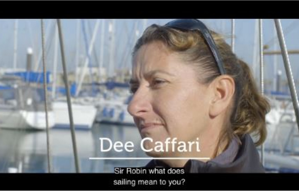 A close-up of a person with sunglasses on their head and boats in the background. Text on screen: 