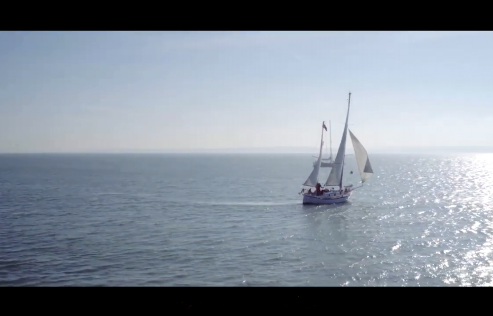 A sailboat with white sails glides on a calm sea under a clear, blue sky.