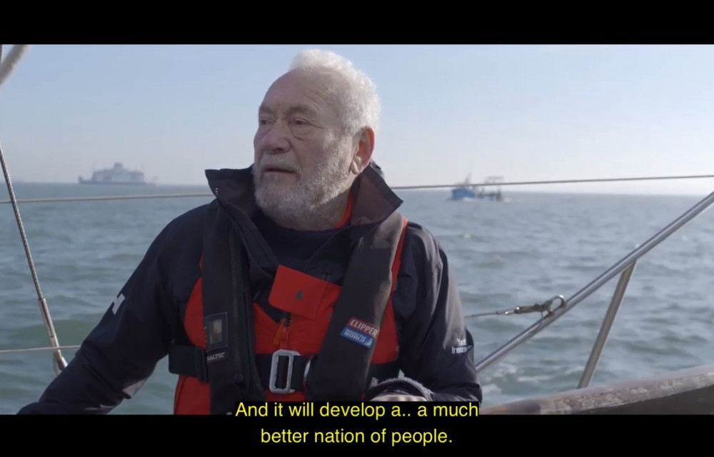 An older man in a life jacket stands on a boat in open water, with subtitles reading, 