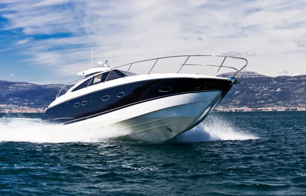 A black and white motor yacht cruising on open water with mountains and a cloudy sky in the background.