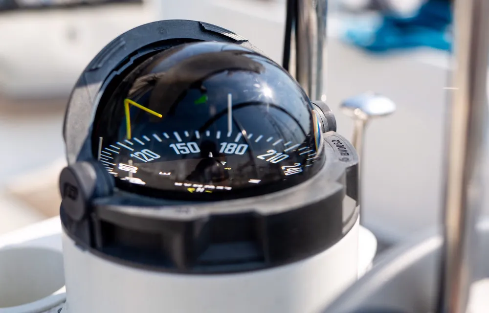 Close-up of a boat's compass, showing a heading of approximately 185 degrees, with reflections visible on its glass dome.