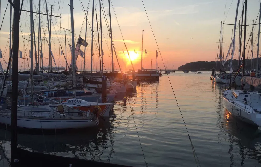 Sunset over a harbor with numerous boats docked, creating a serene reflection on the calm water.