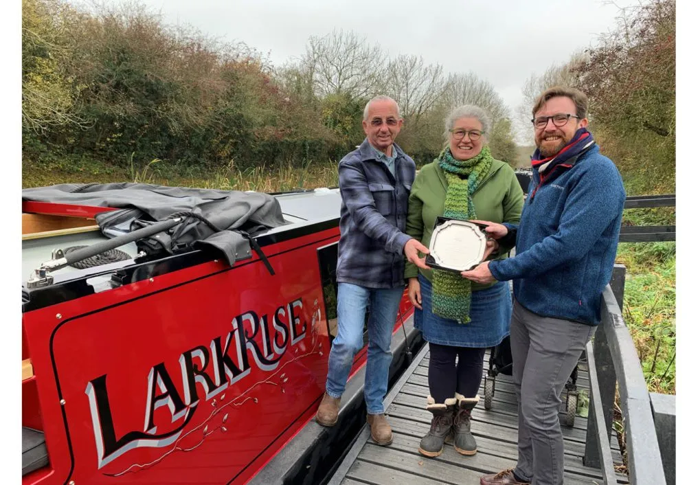 Three people standing by a red boat named 