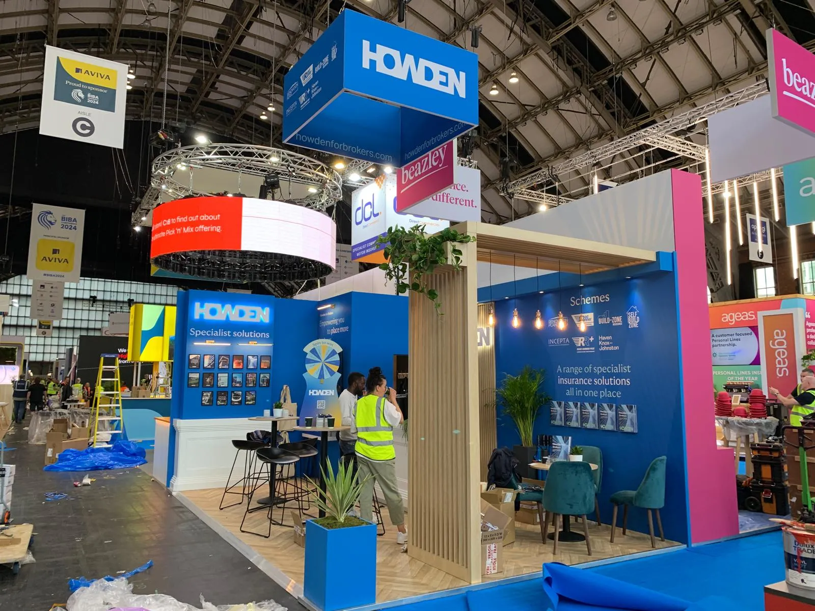 Howden exhibition stand at a trade show. Displays promotional materials and seating area with attendees setting up.