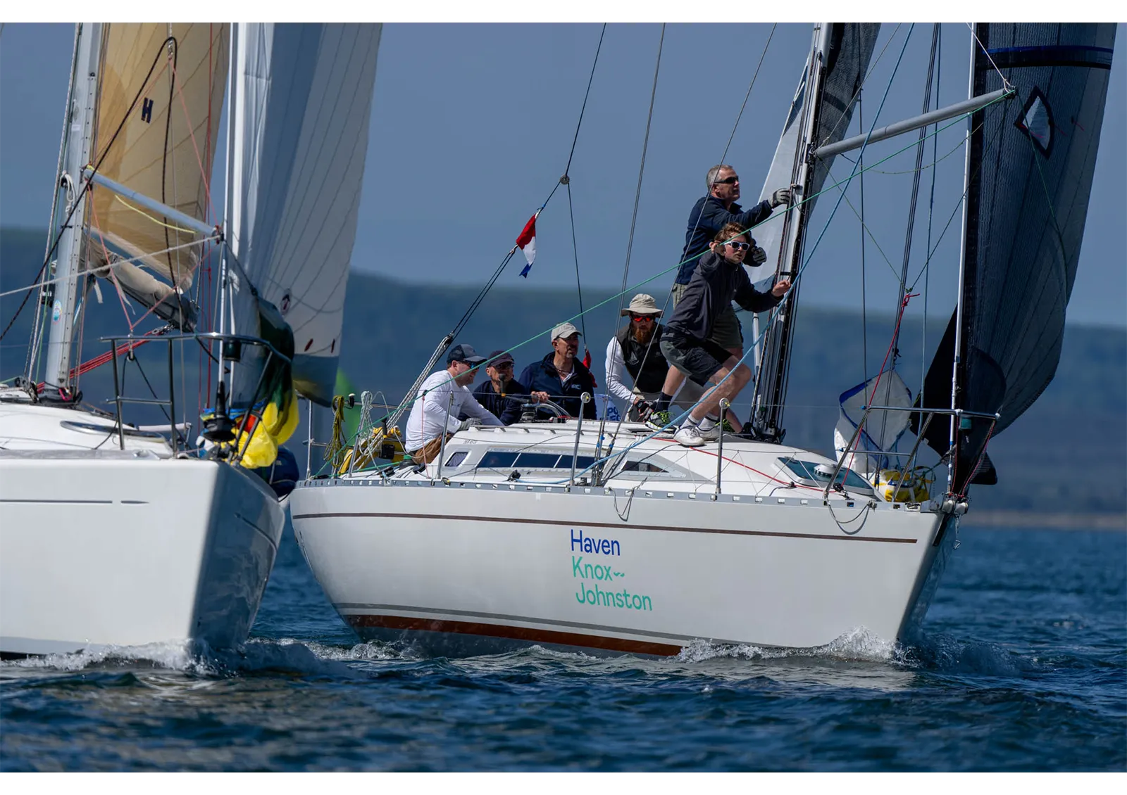 Sailors maneuver two sailboats close to each other on a clear day, concentrating on adjusting the sails and ropes.