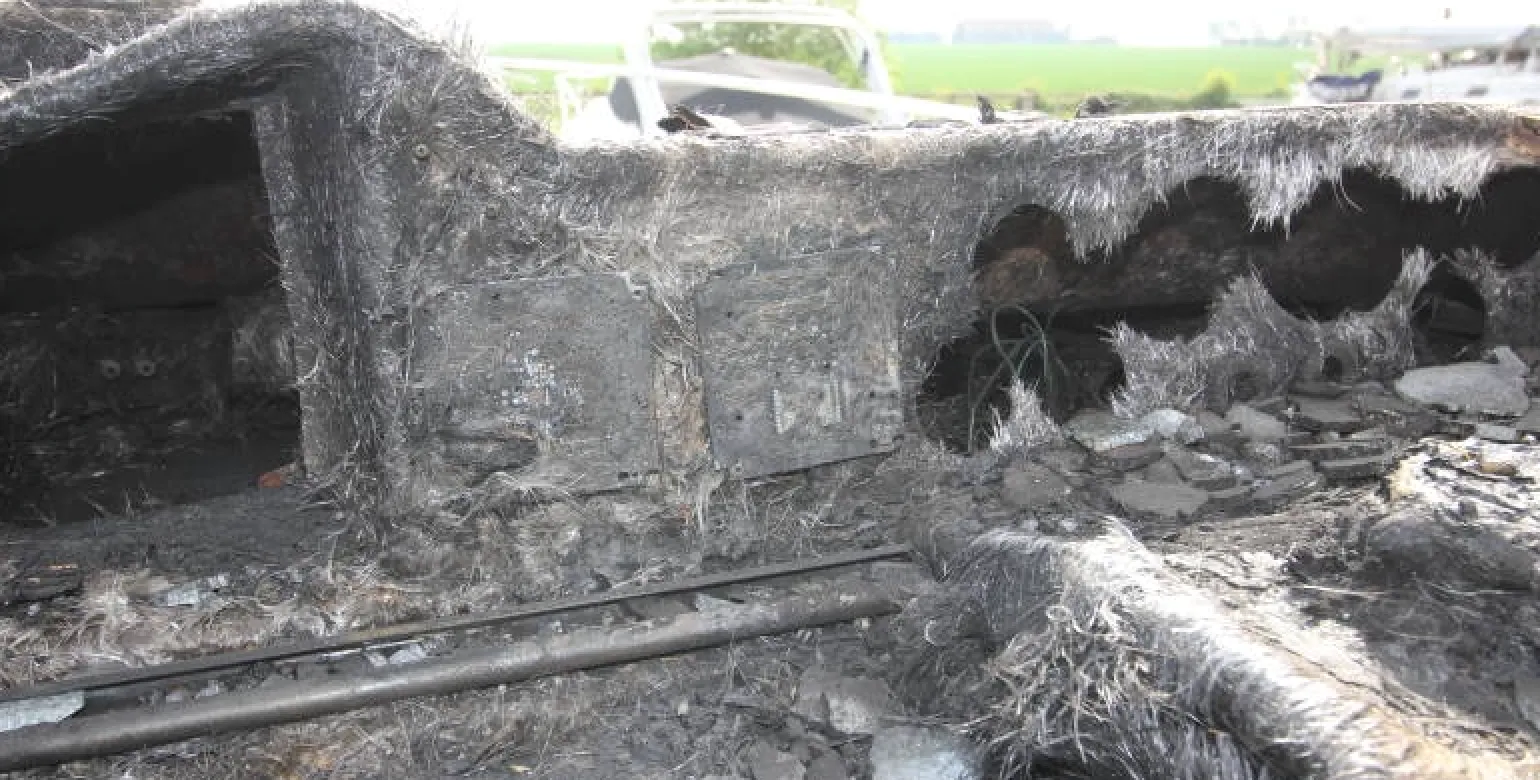 Close-up of the charred interior of a burnt vehicle, showing extensive fire damage and exposed structural elements.