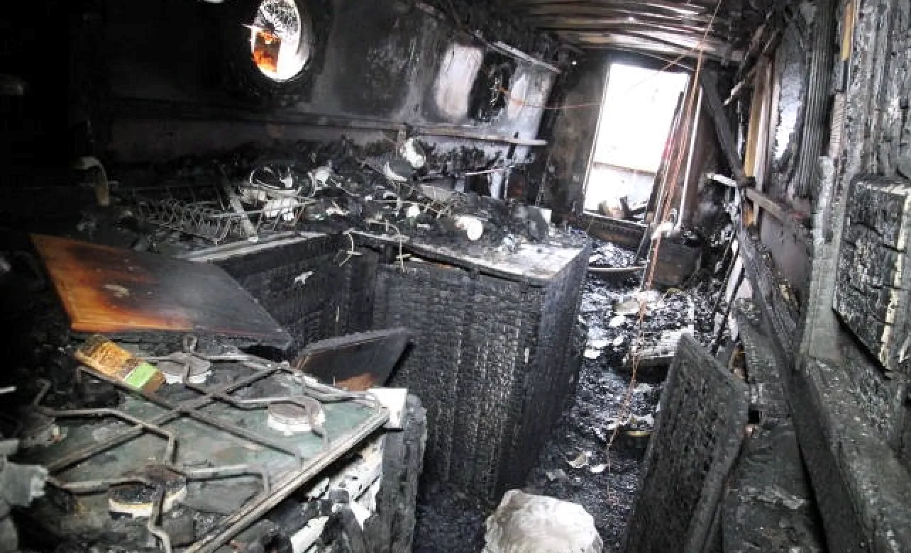 Interior of a burned, charred room with debris and soot covering the surfaces, showing extensive fire damage.